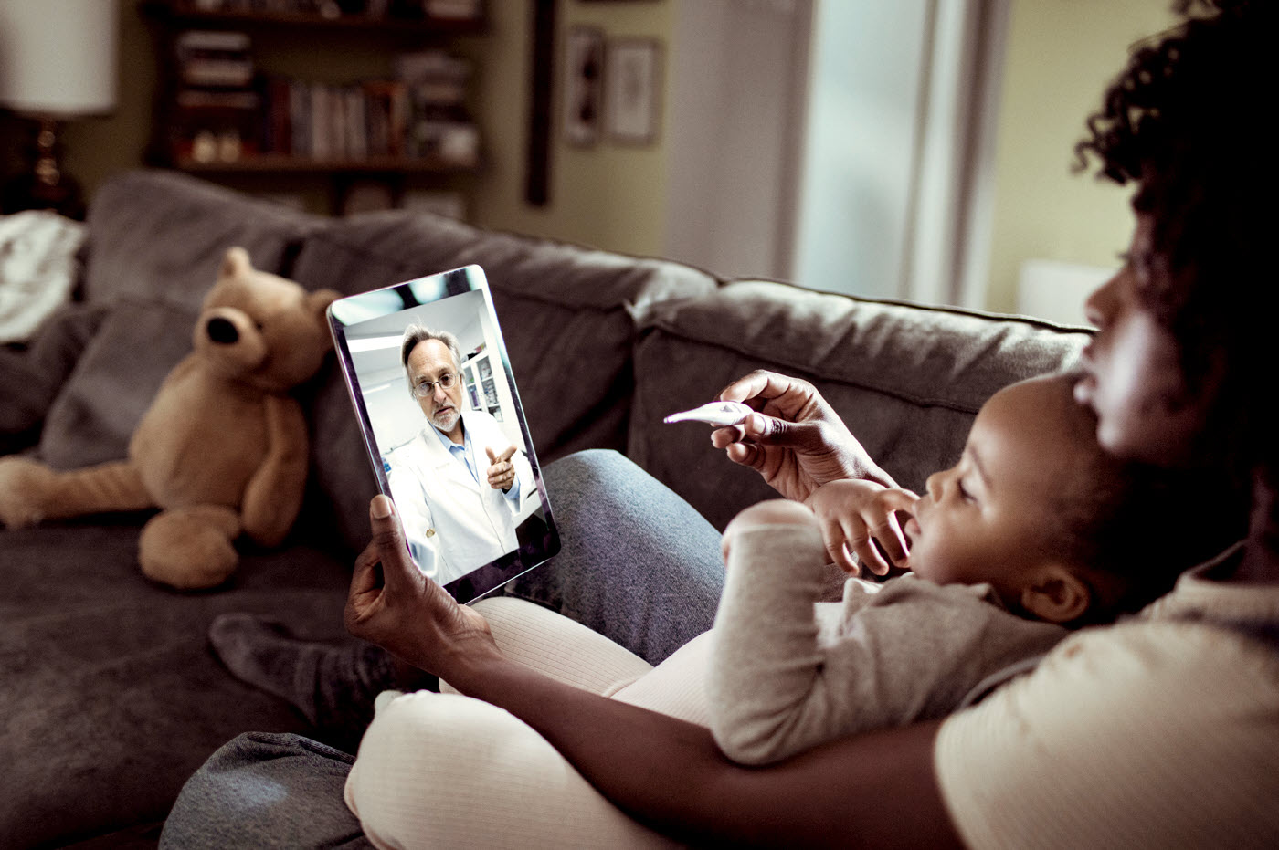 A mother and son in a virtual health meeting on a tablet device with a doctor