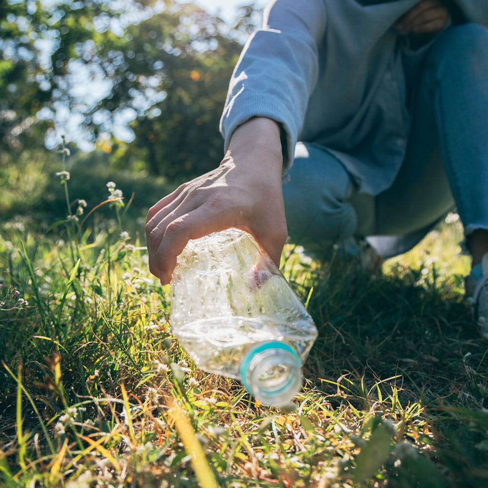 A person picking up a plastic bottle off the ground. 