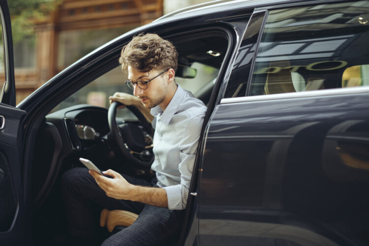 A man getting out of a car while looking at a smart phone.