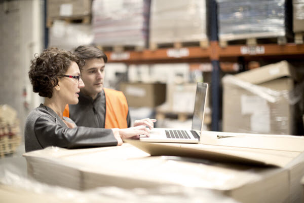 Two people working on a laptop in a warehouse.