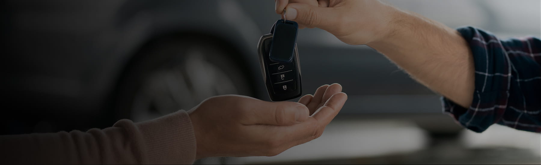 Someone handing a person a set of keys in a car dealership, desktop hero.