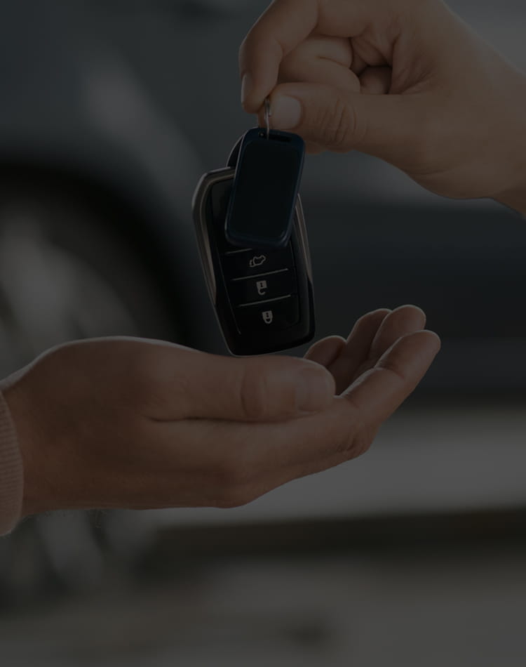 Someone handing a person a set of keys in a car dealership, mobile hero.