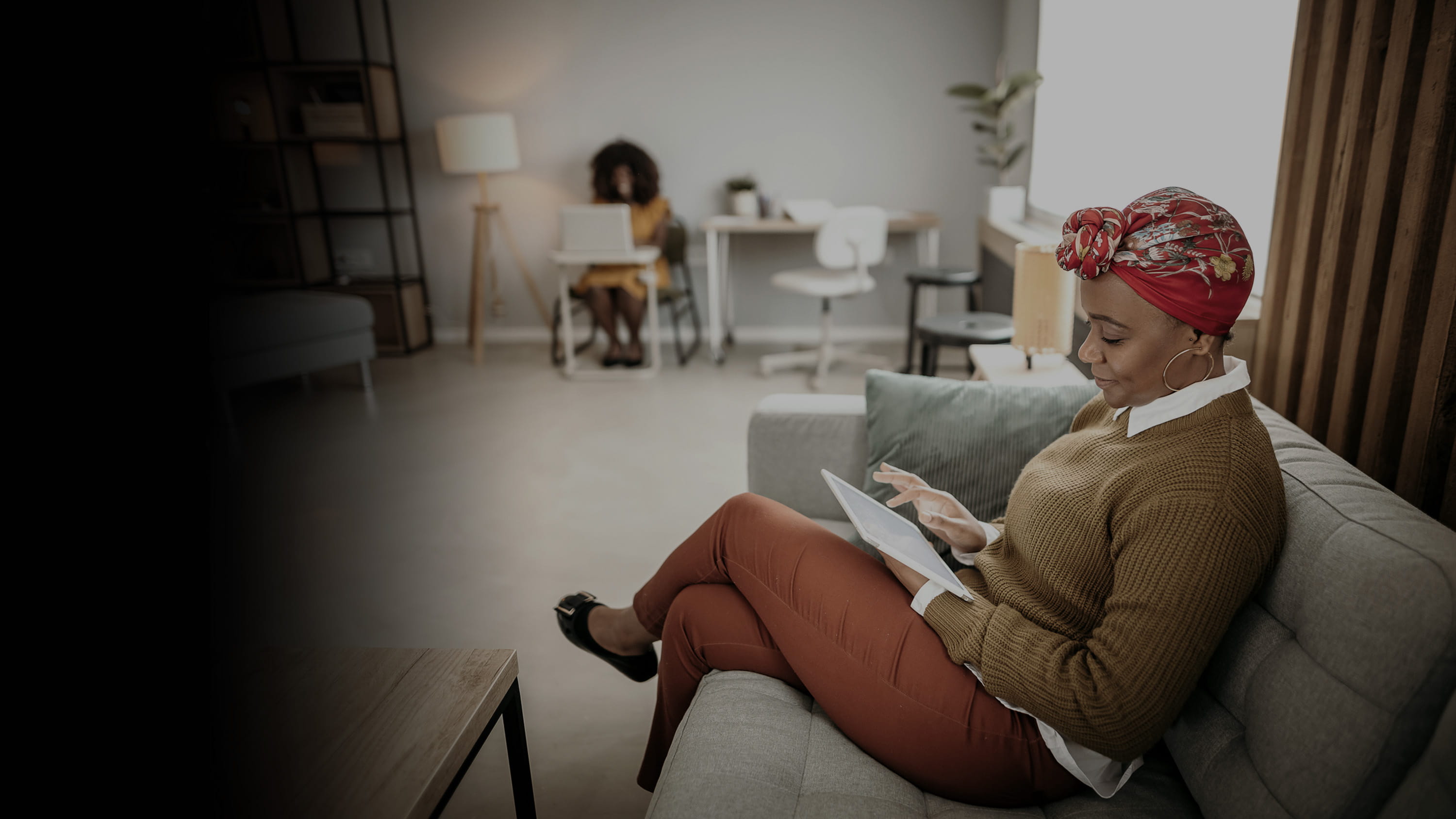 A woman working on her tablet device while sitting on the couch.