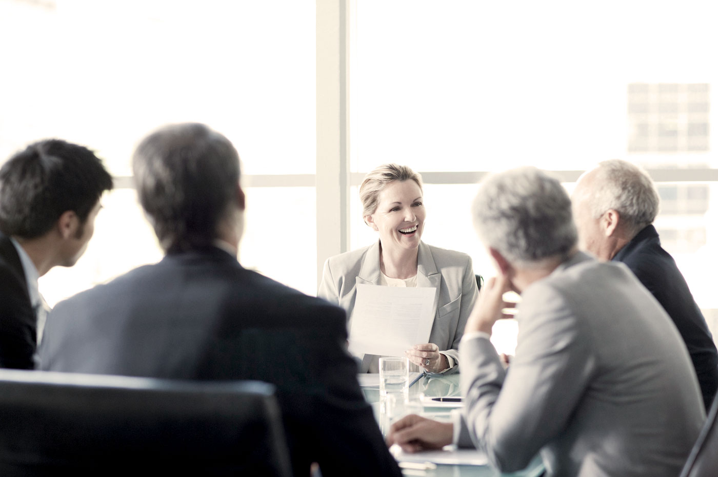 A group of business people sitting around a conference table talking and smiling.