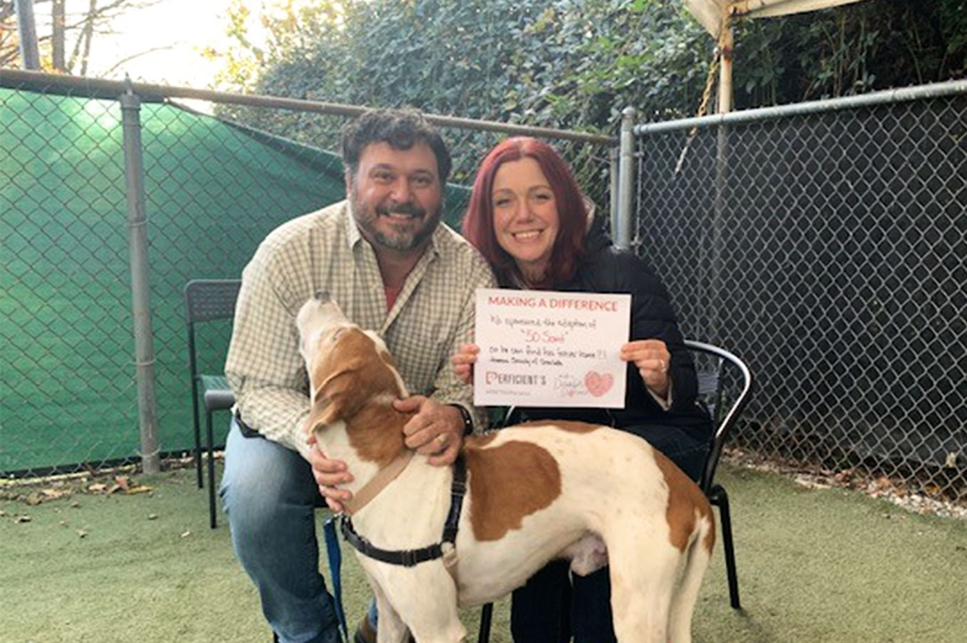 A colleague and his wife with a dog and holding a MADD sign for dog adoptions.
