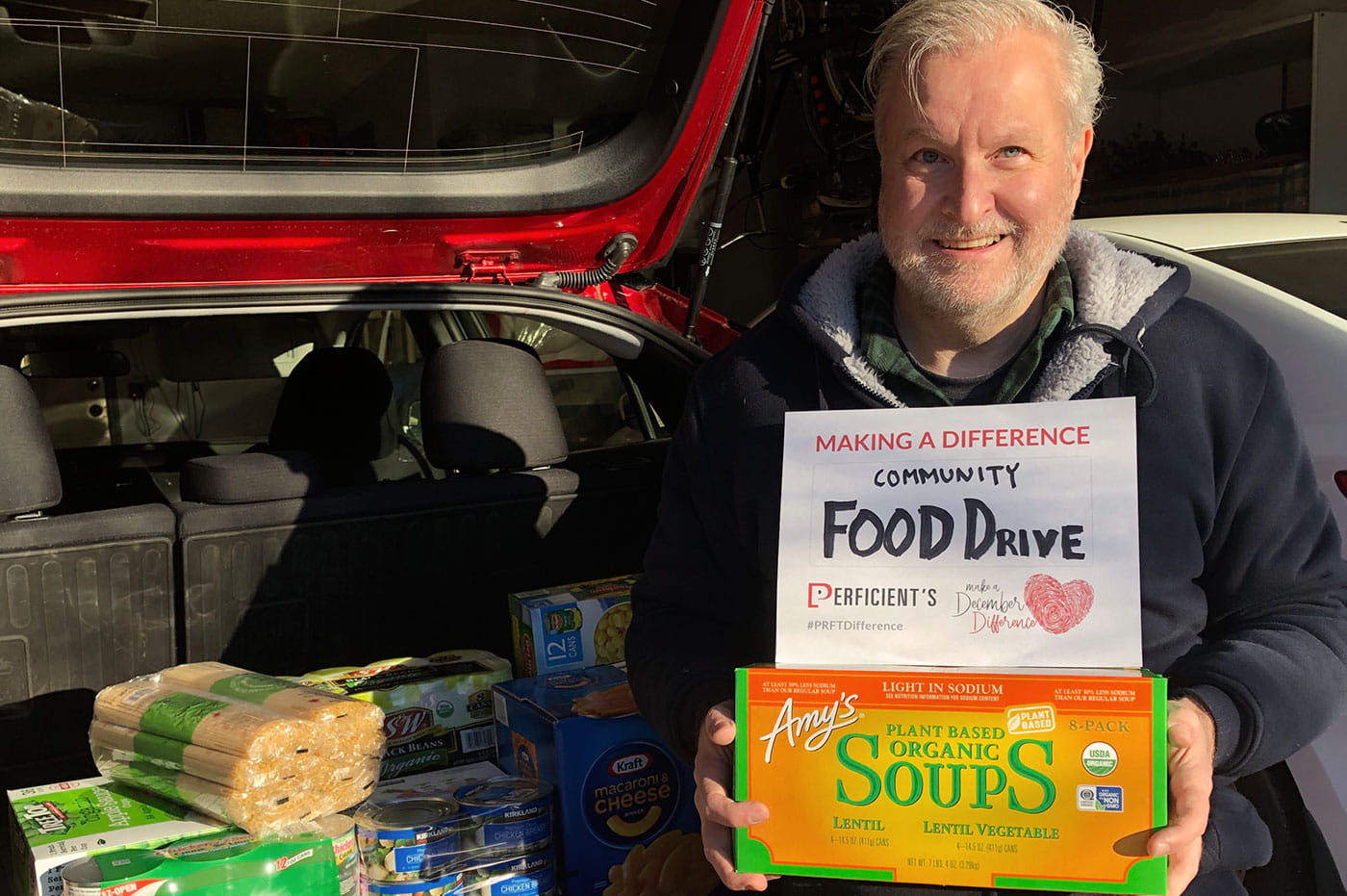 A colleague holding MADD sign and food donations for a community food drive.
