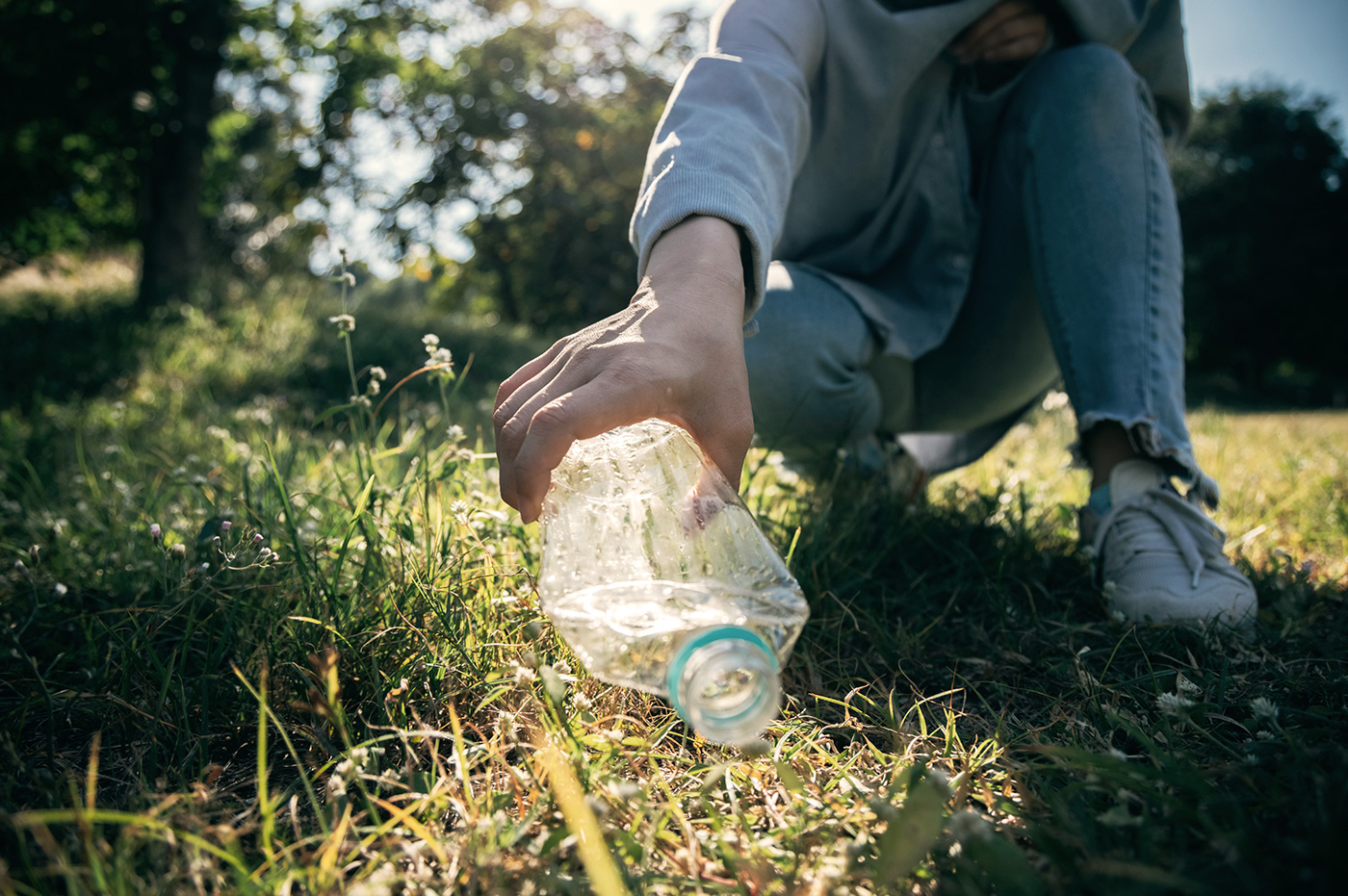 Person picking up an empty and crushed water bottle that was sitting in the grass.
