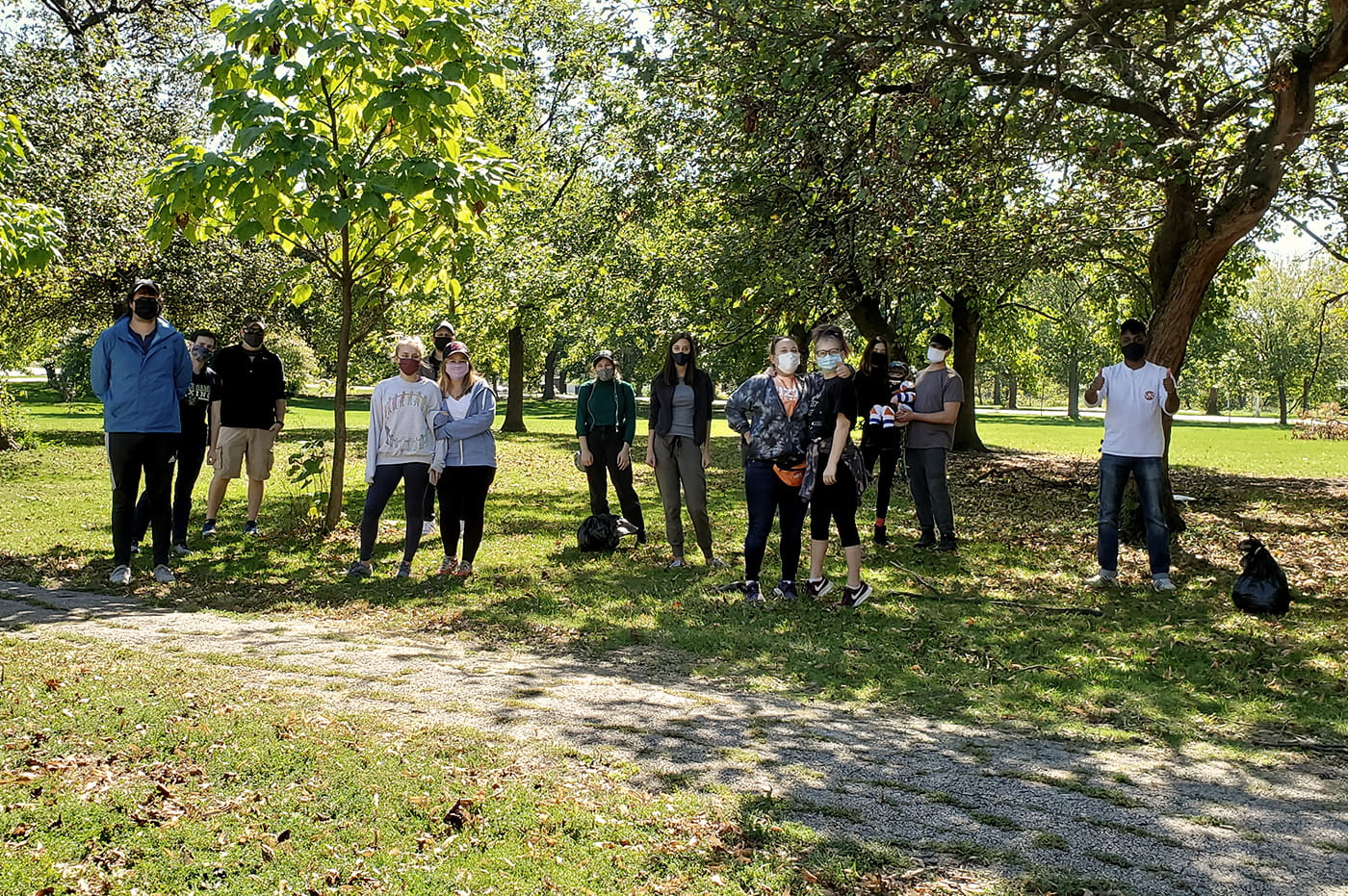 A large group of masked people cleaning up litter in a park. 