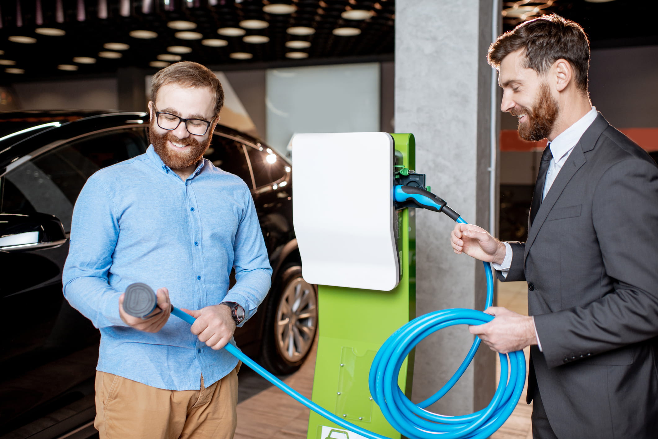 A car dealership man showing another man how to use an electric charging port for an electric vehicle 