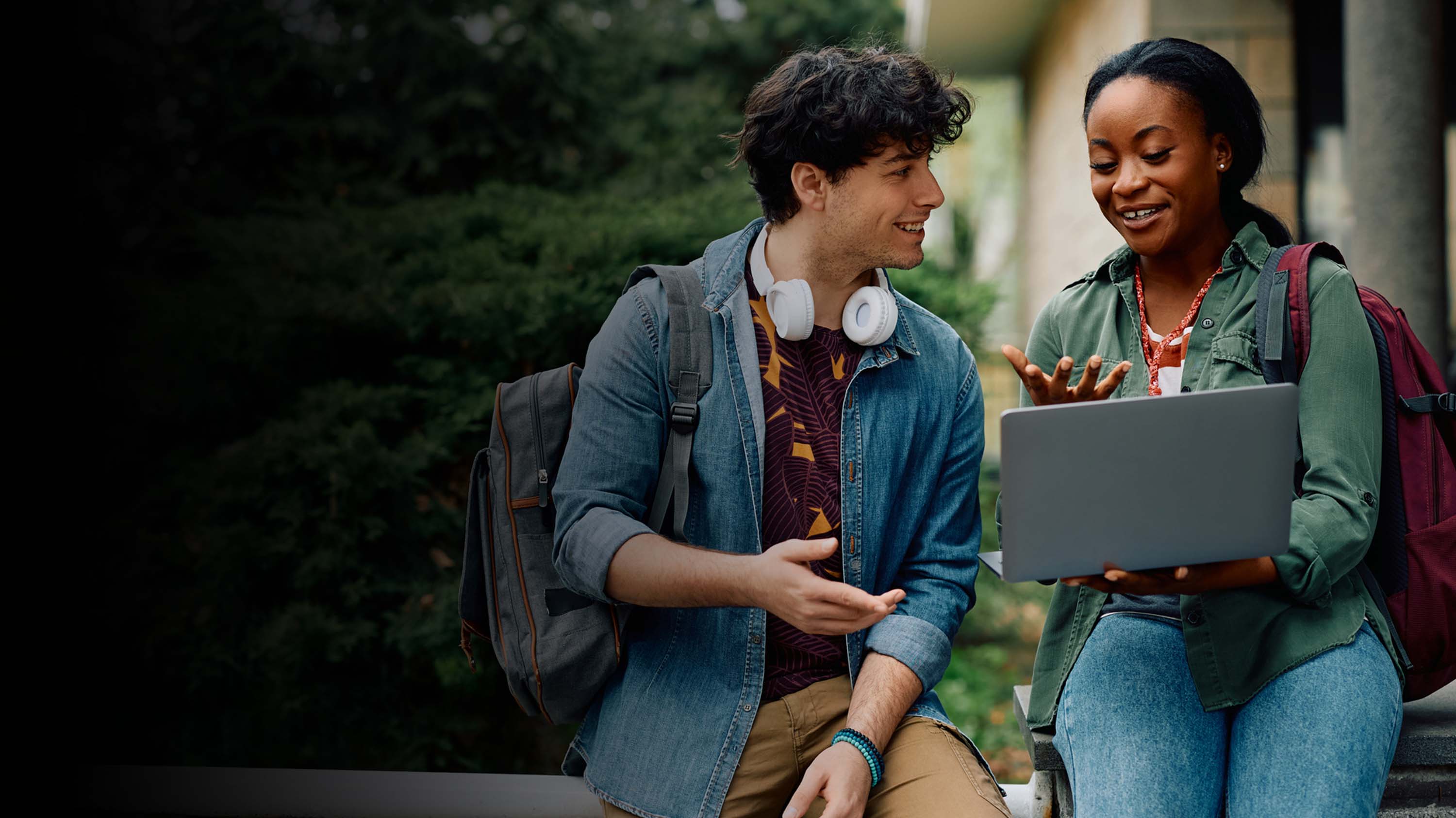 A woman and a man college students talking and one is holding an open laptop