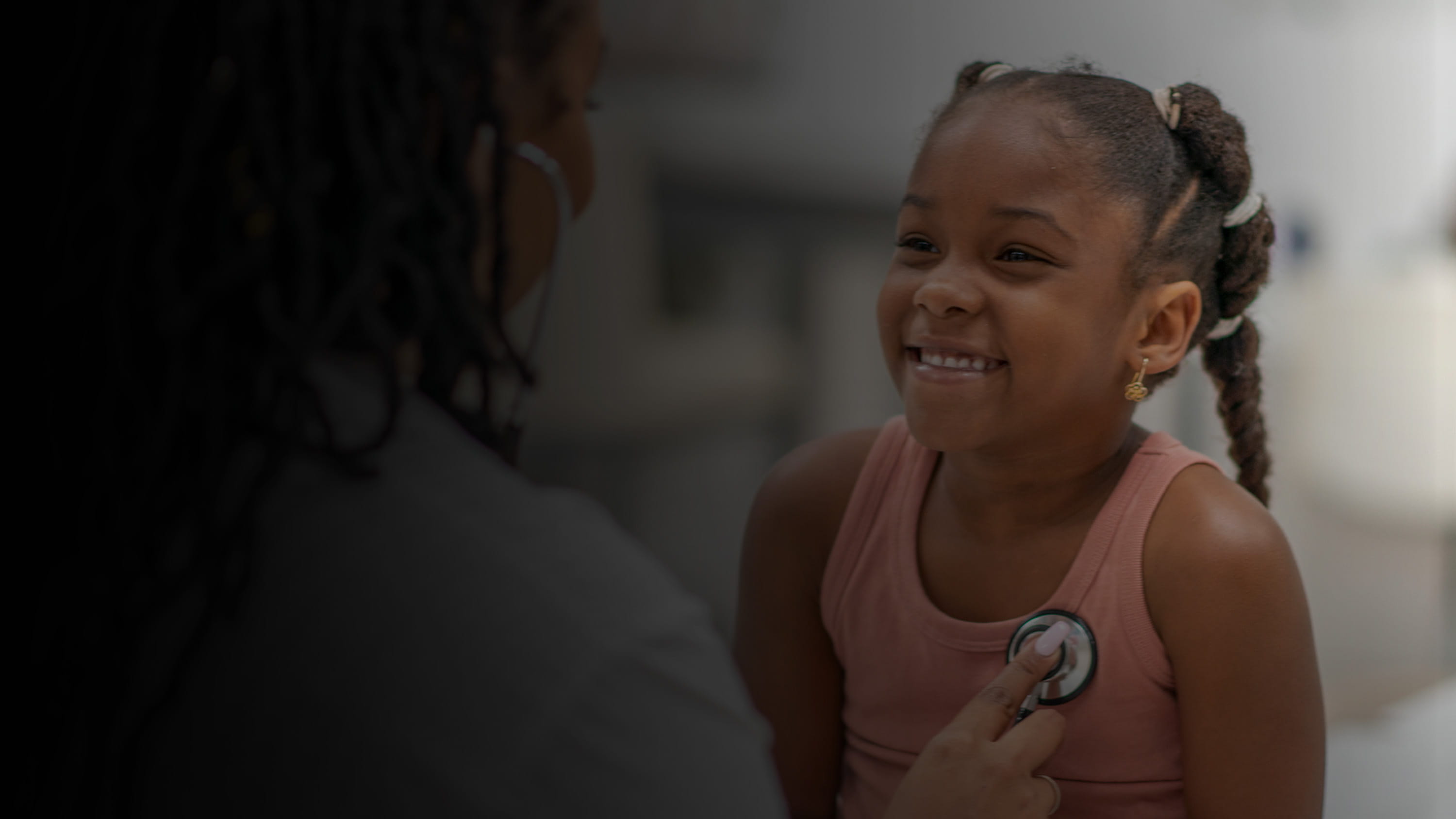 A doctor using a stethoscope to listen to a little girl's heart.