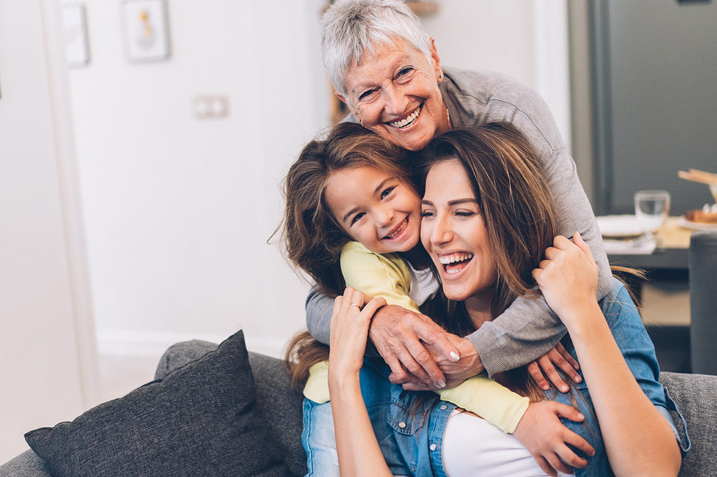 Grandmother, mother, and daughter hugging and smiling.