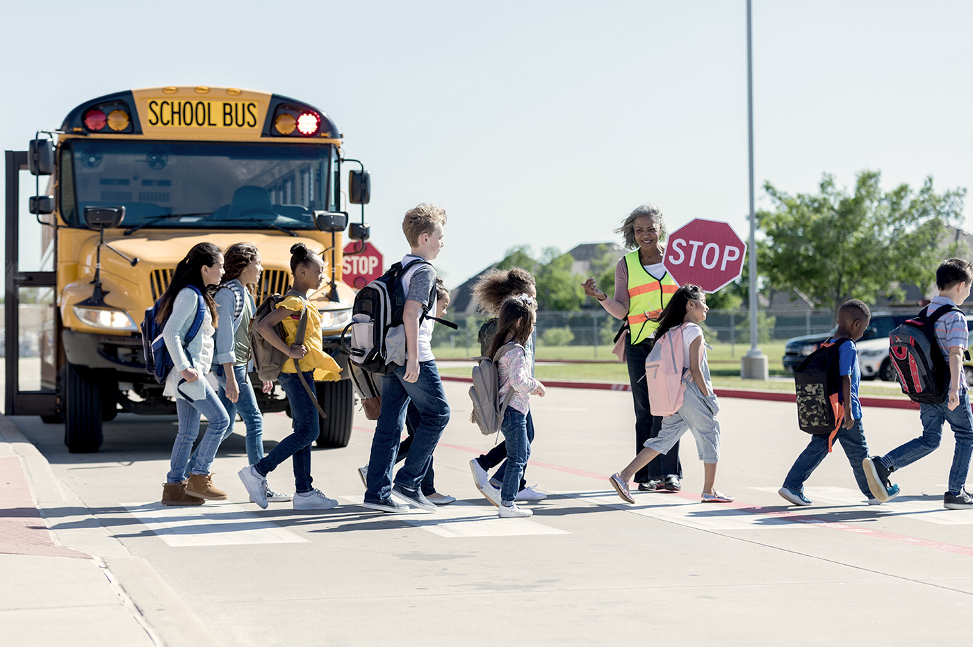 Children crossing the street with a crossing guard in front of a school bus.