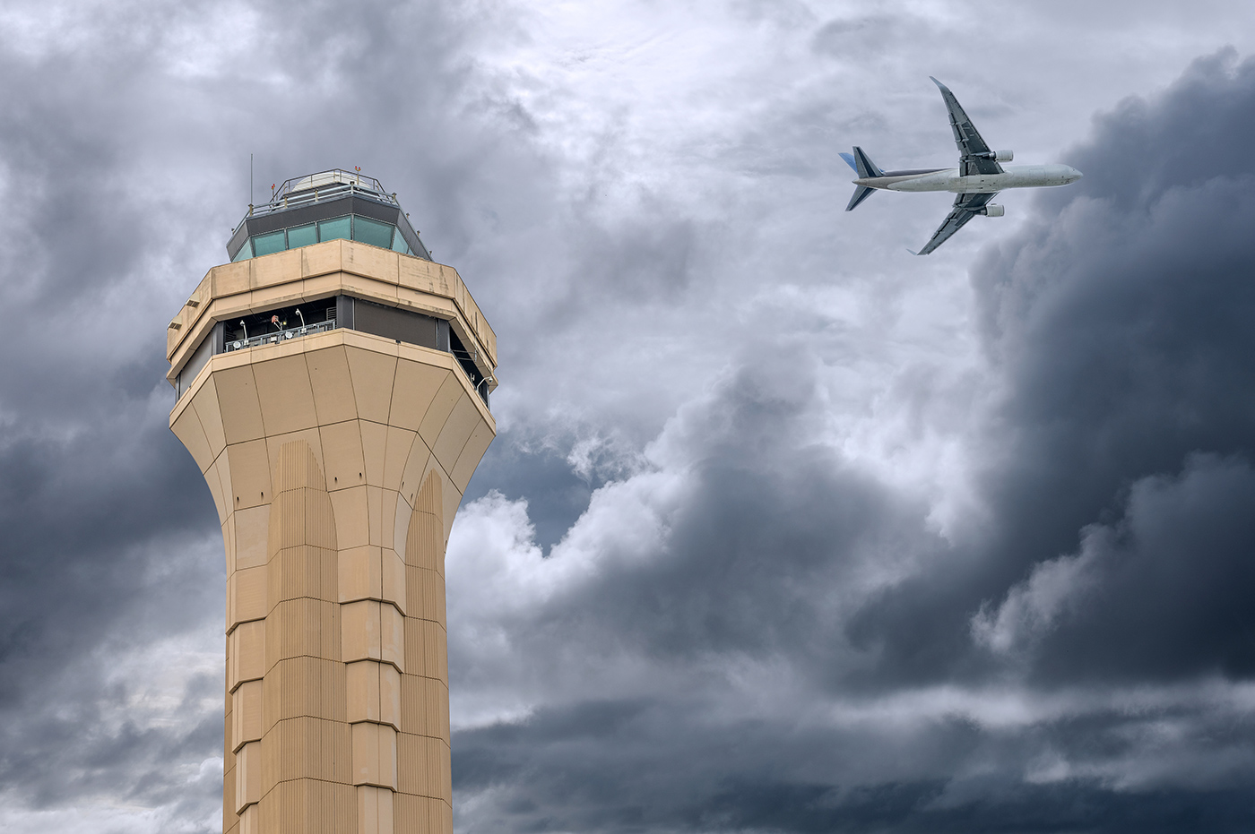 Airplane flying over air traffic control tower in cloudy skies.