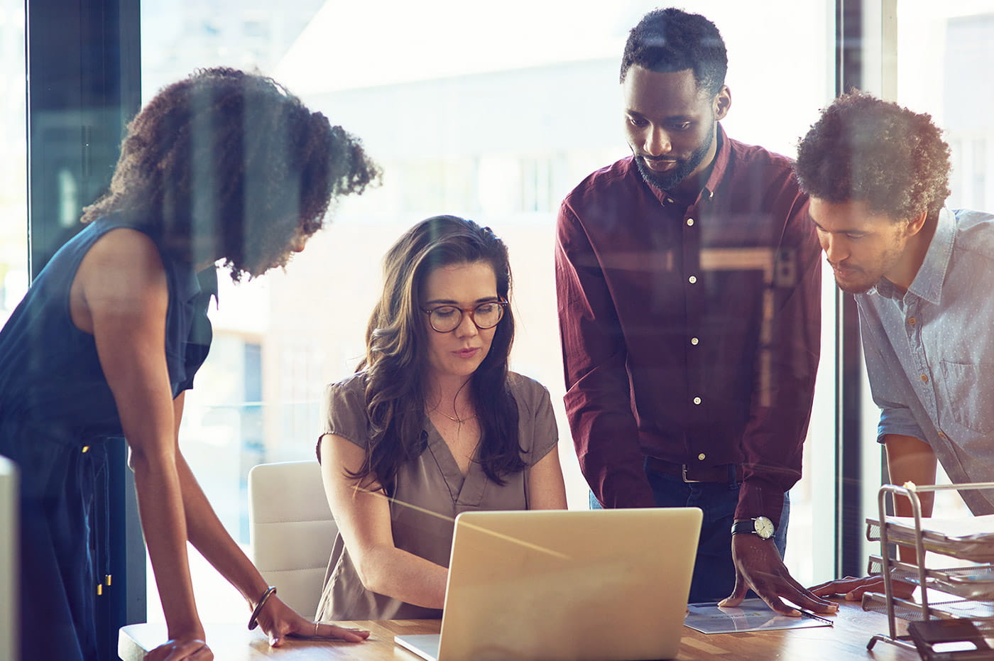 Group of professionals gathered around a table looking at a laptop.