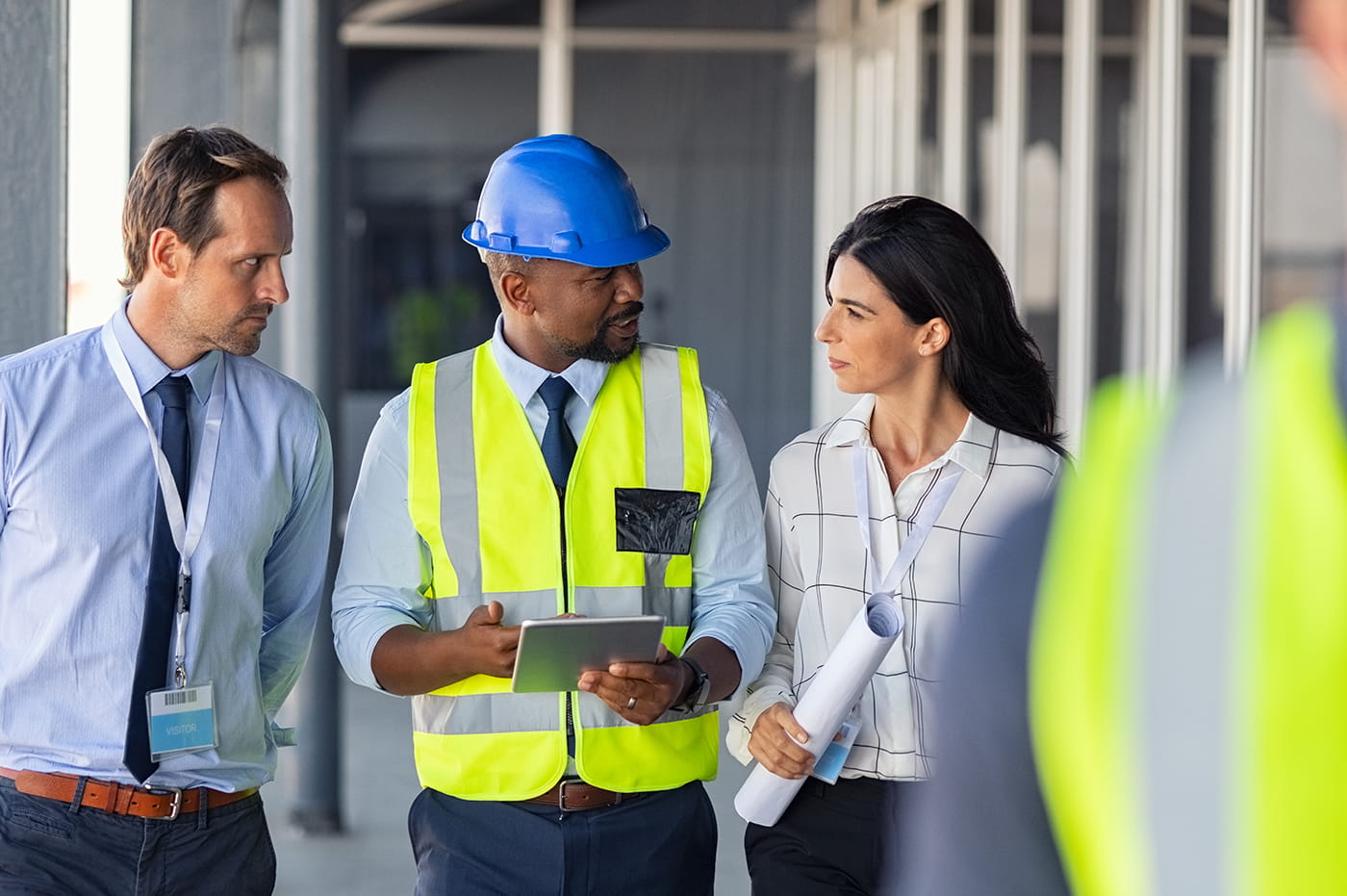 Three people walking and discussing, one person wearing a yellow vest and construction helmet.