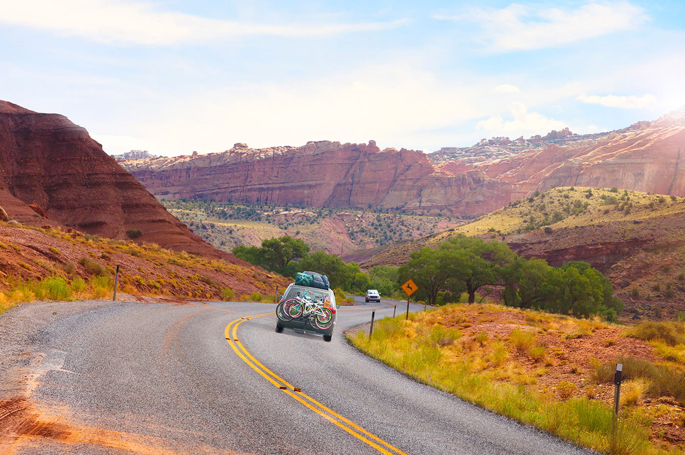 Car with bikes and camping gear driving on a canyon road.