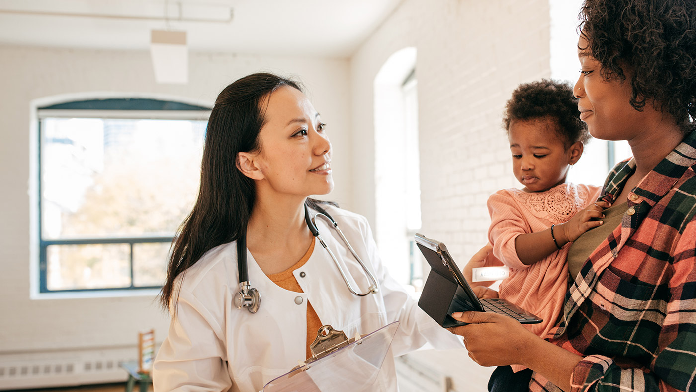 Female doctor talking with a mother and daughter who are holding an iPad.