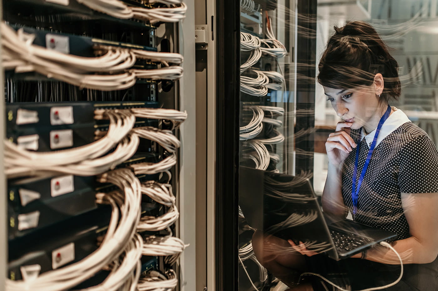 Woman looking at laptop and working on a large computer server.