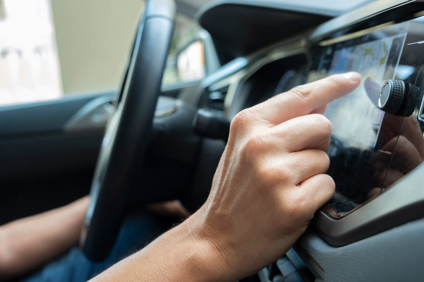 Person in front seat of a car tapping touch-screen radio.