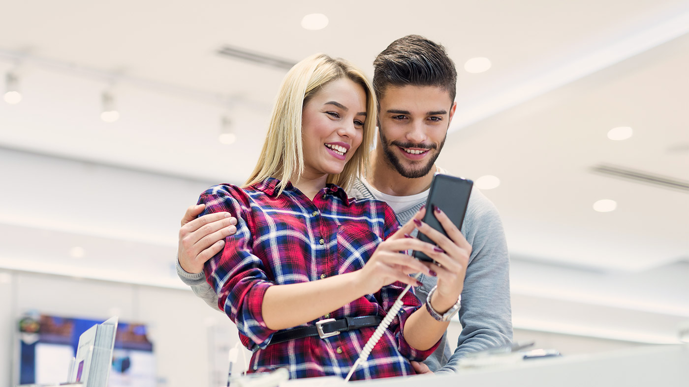 Two people looking at a cell phone in a store and smiling.