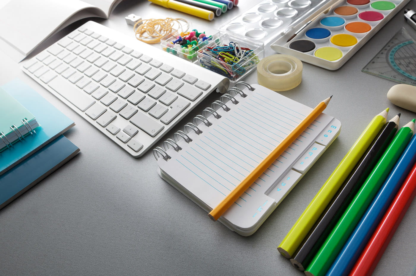 Computer keyboard, notebook, and design supplies on a desk.