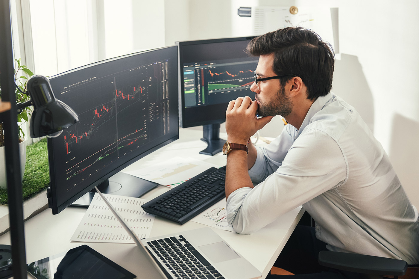 A man looking at data sets displayed on two curved monitors.