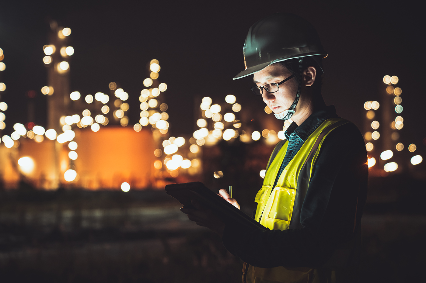 Man in vest and helmet working on an iPad in front of a lot of lights at an energy plant.