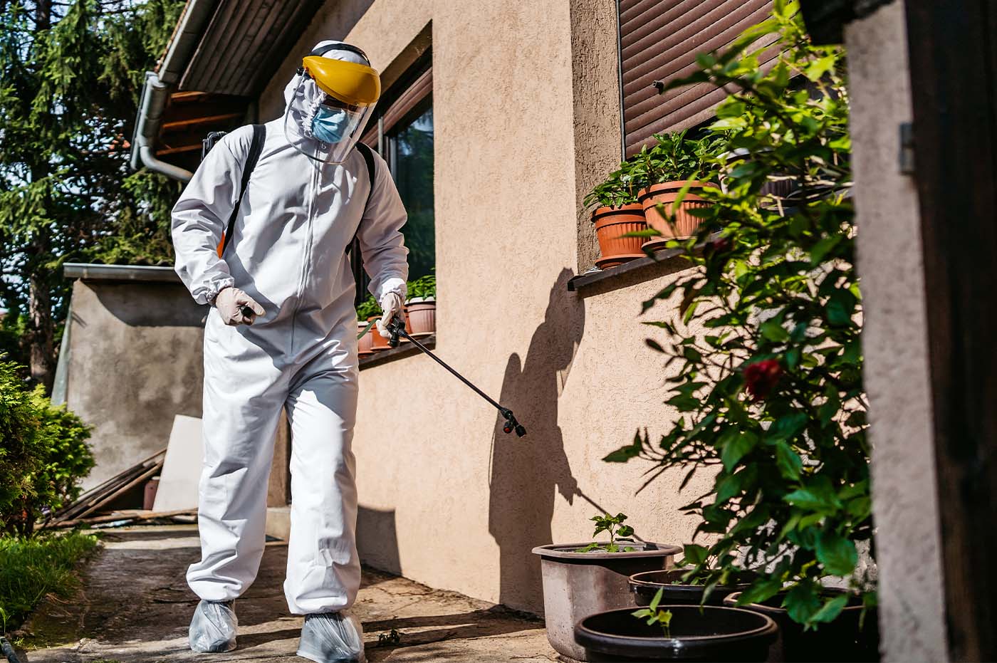 Person in a hazmat suit and mask spraying liquid on the outside of a house.