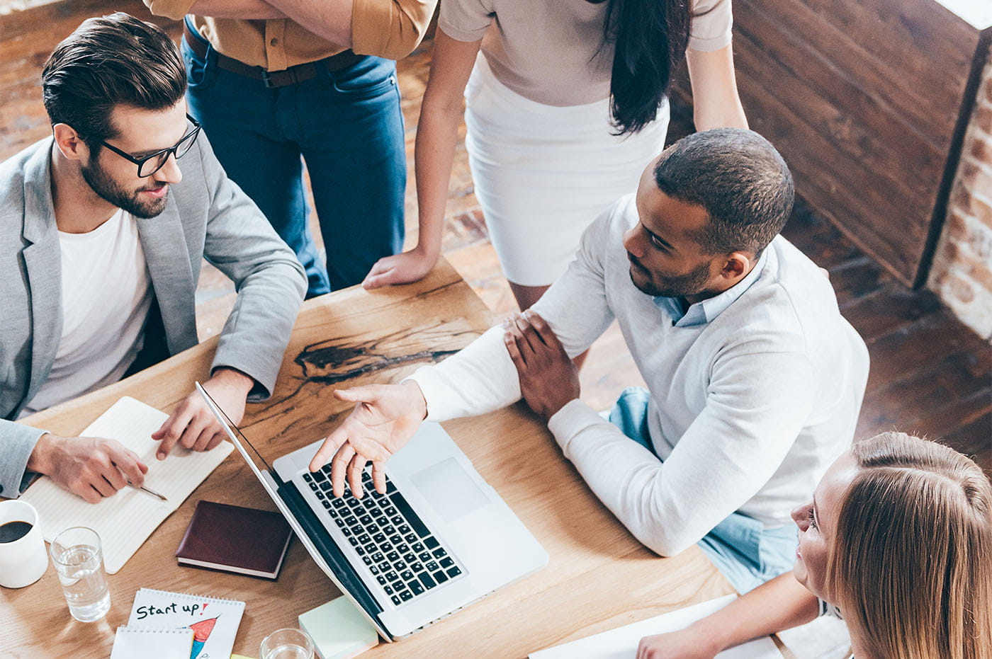 Several business people gathered around a laptop and working.