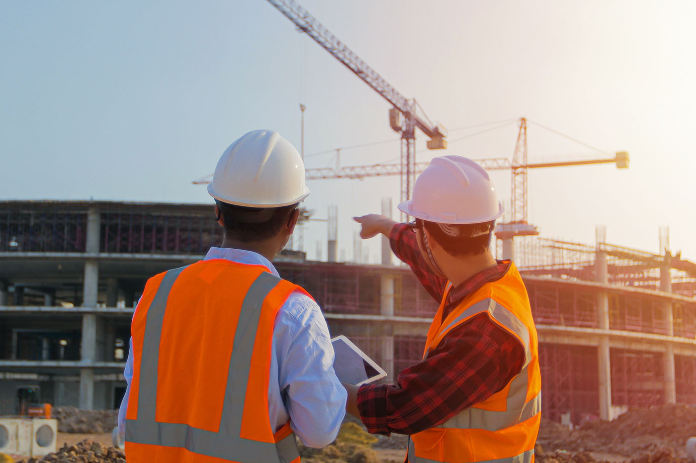 Two men in hard hats and safety vests talking at a work site.