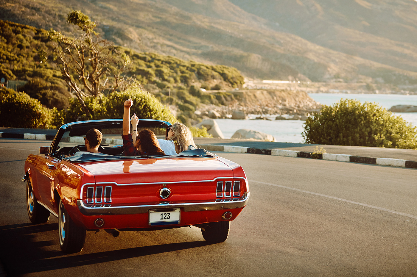 Three people driving down a coastal road in a convertable.