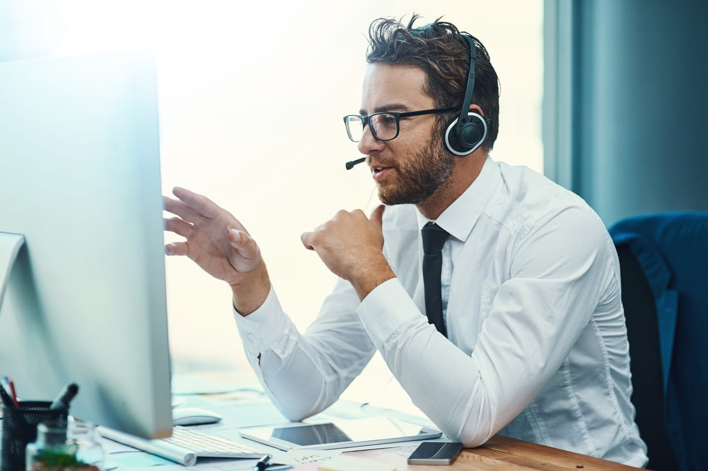 A man sitting at a computer and talking on a headset.