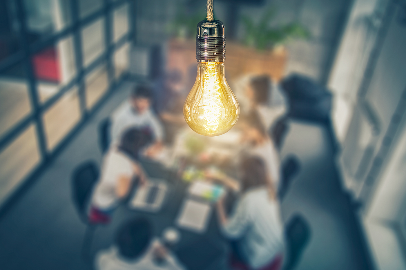 Illuminated lightbulb hanging over a conference table full of people talking.
