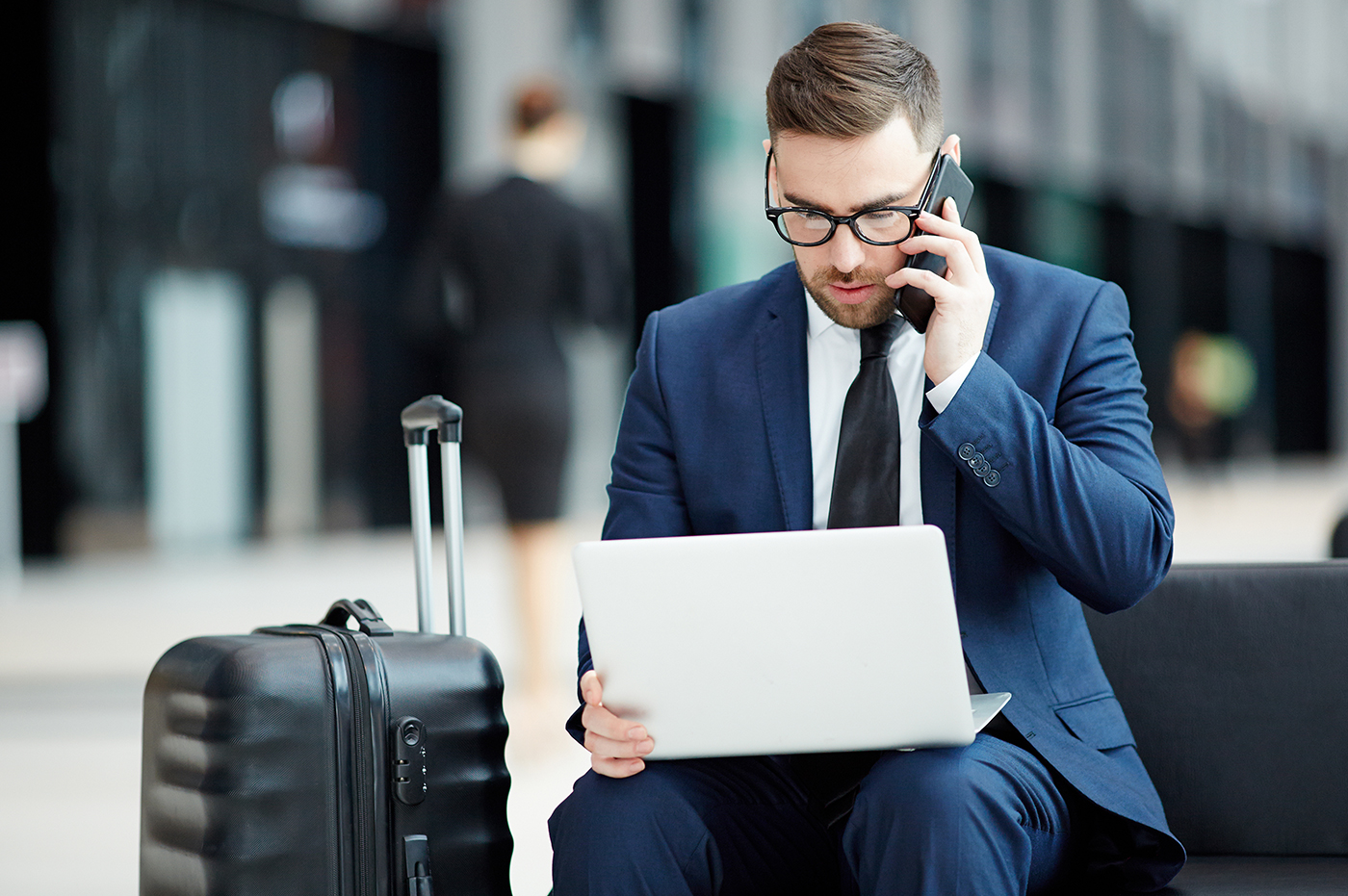 Business man in an airport working on laptop and talking on phone.