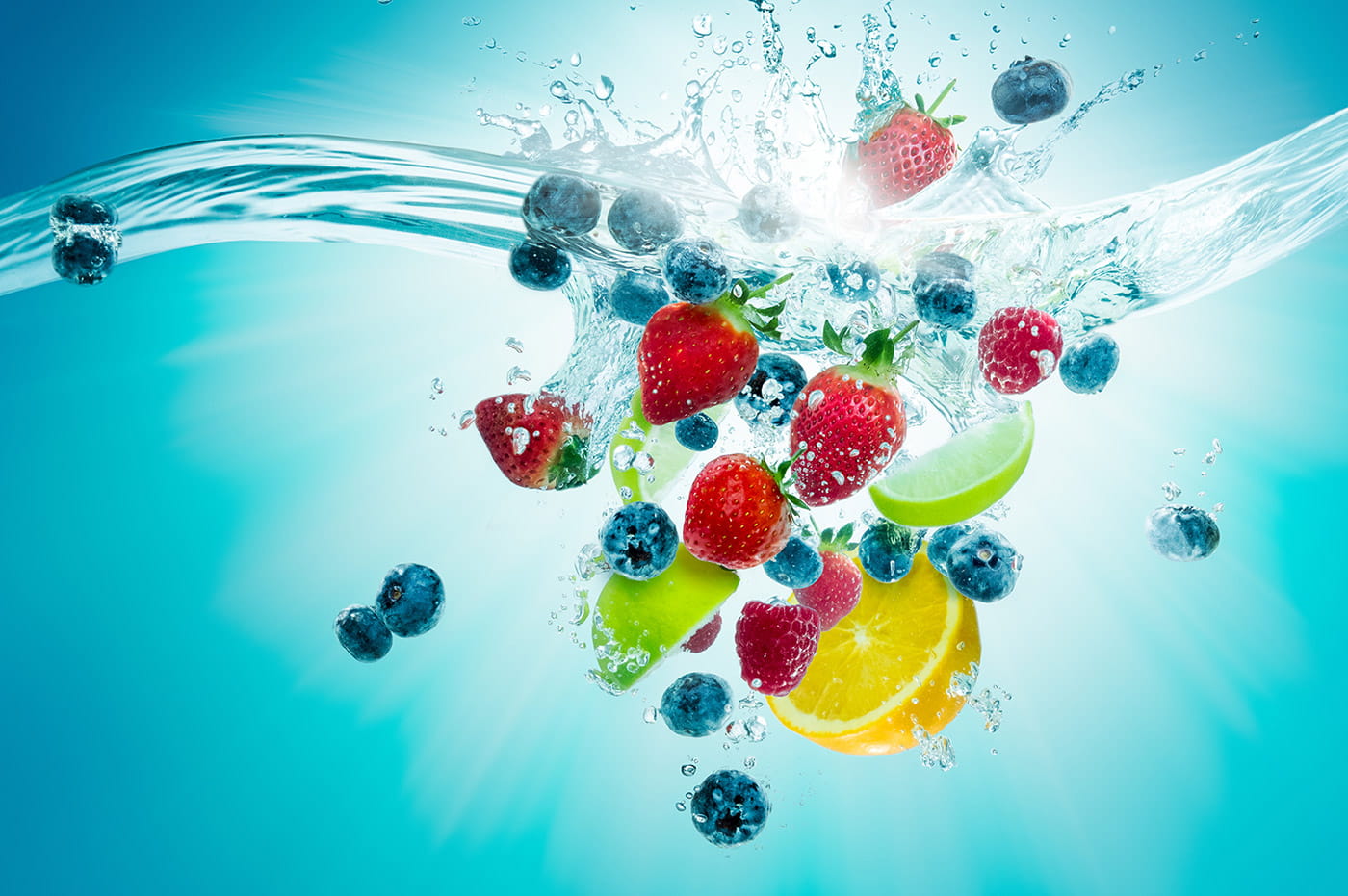 Strawberries, blueberries, and citrus spashing into water on a blue background.
