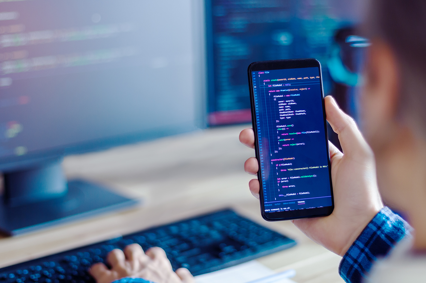 Man working with technical code on cellphone and desktop computer.