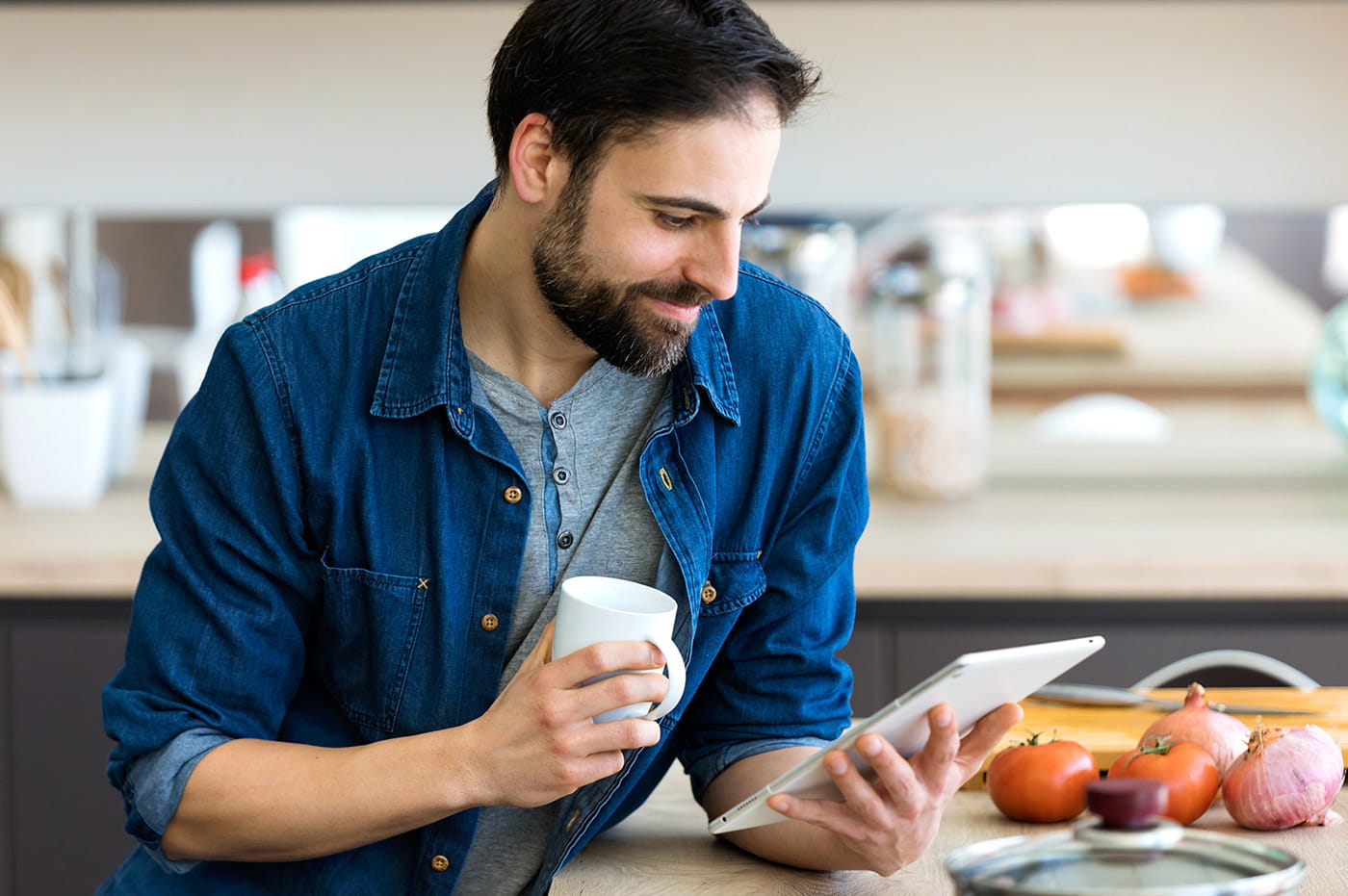 Man sitting at a kitchen counter with vegetables and looking at an iPad.