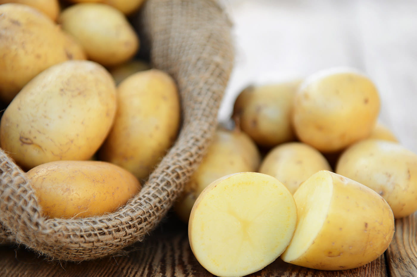 Burlap sack full of potatoes, with one potatoe cut in half.