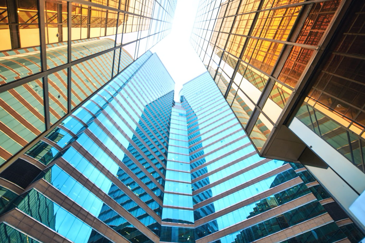 Seveal glass skyscrapers clustered together with sun shining through them.