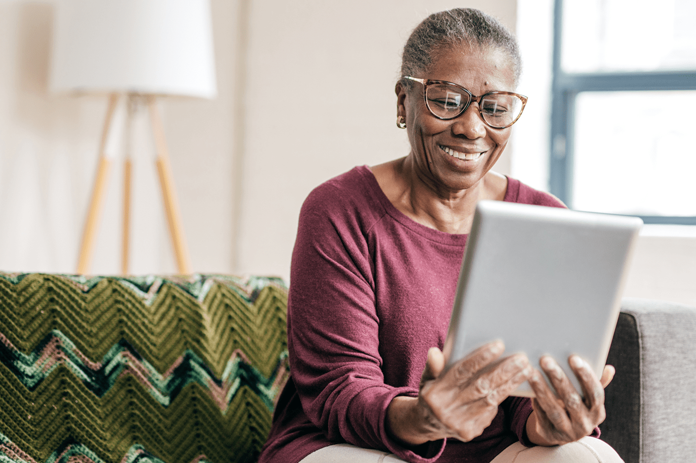 An older woman sitting on a couch and looking at a tablet.