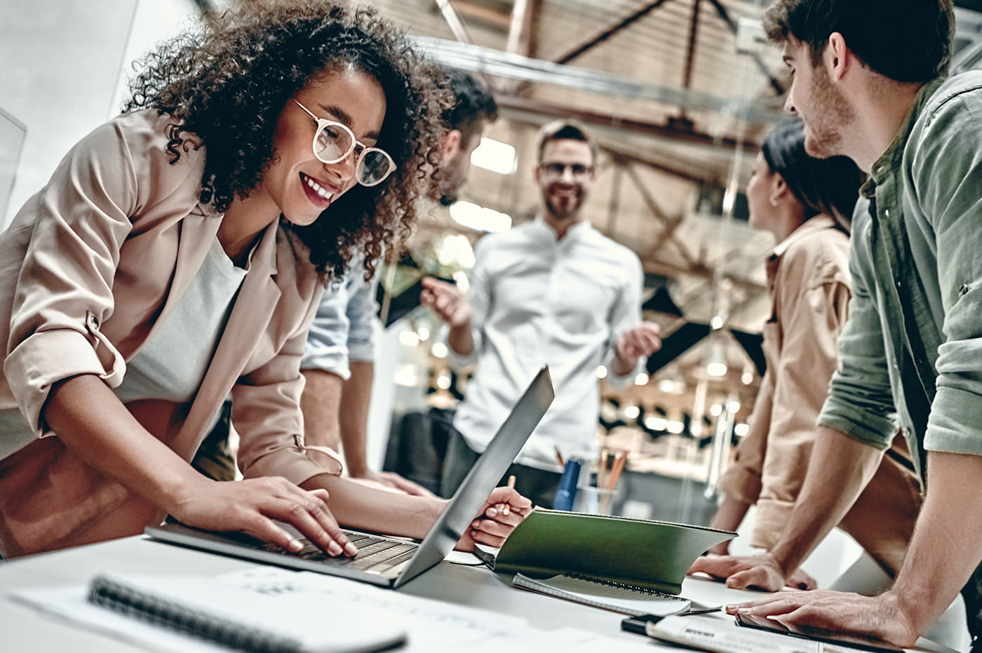 A group of five business people talking with one woman working on a laptop.