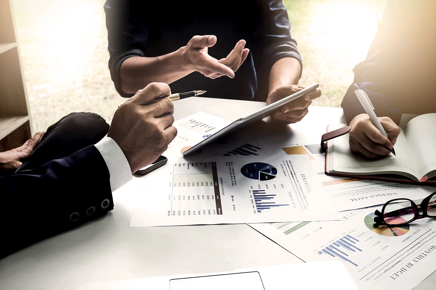 Three people discussing data on and iPad and taking notes.