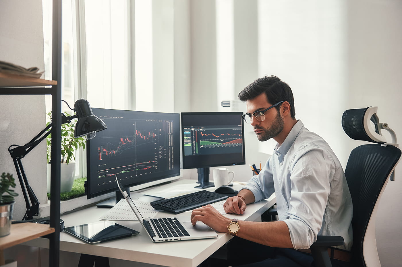 A man working with data on laptop and two desktop monitors.