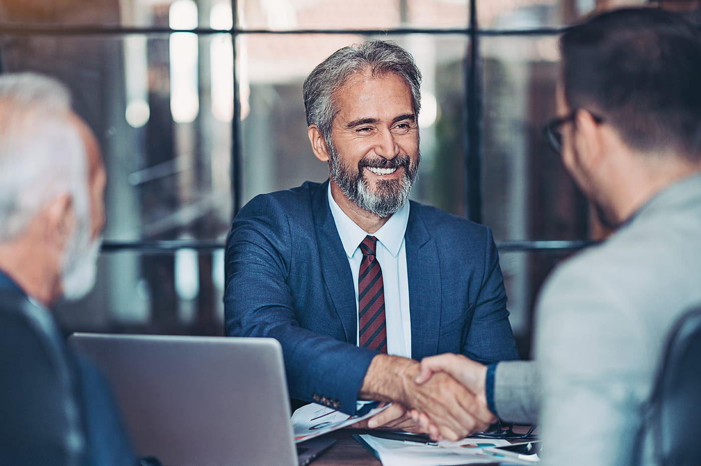 Two older business men and one younger man shaking hands and smiling.