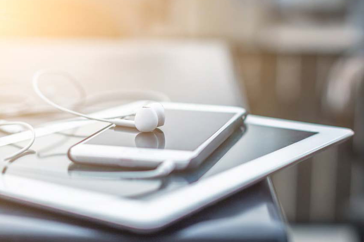 A tablet and smartphone with earbuds stacking on top of one another.