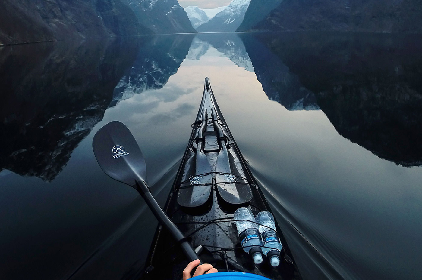 The front of a kayak and paddle in a lake by the mountains.