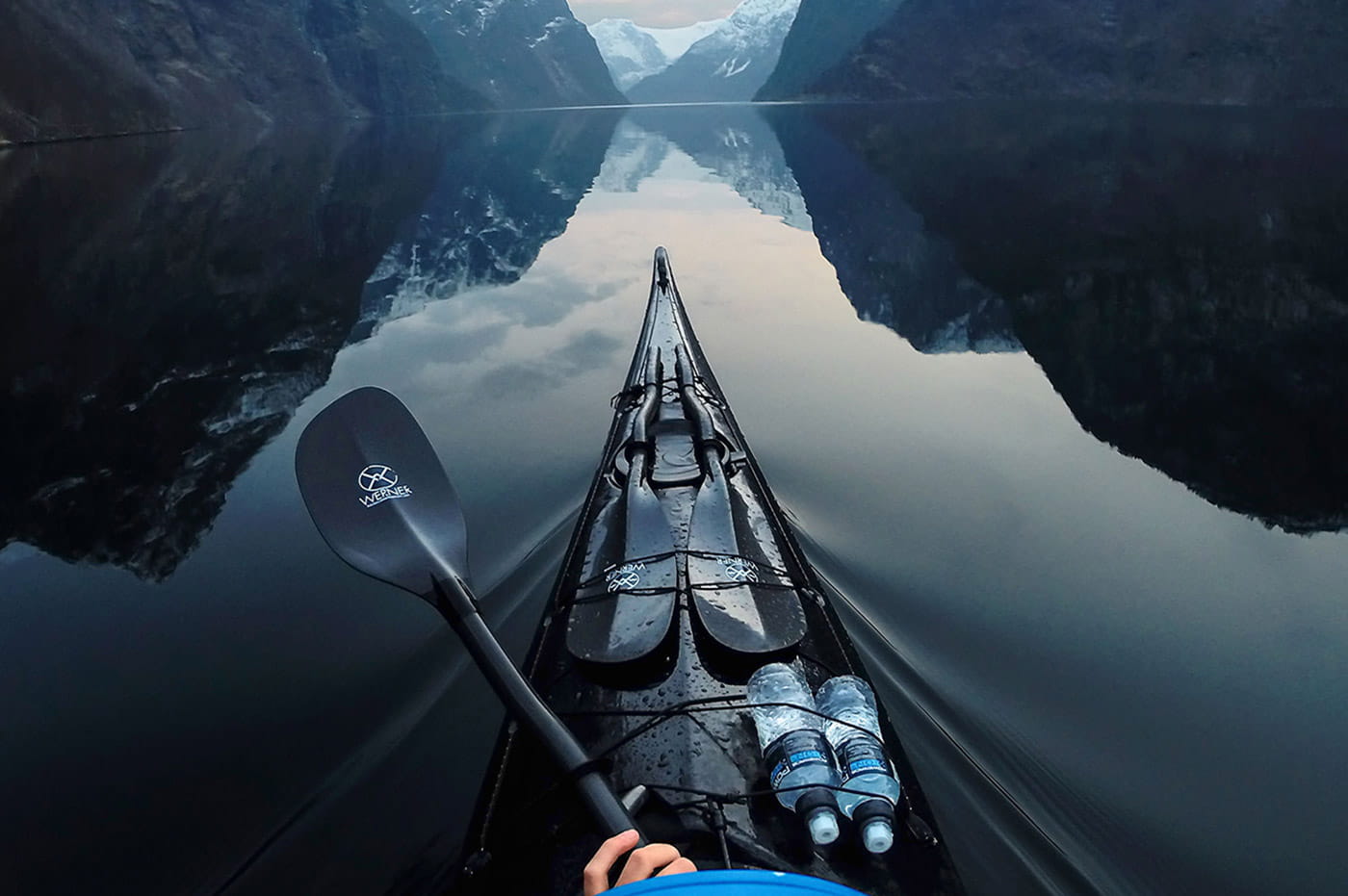 The front of a kayak and paddle in a lake by the mountains.