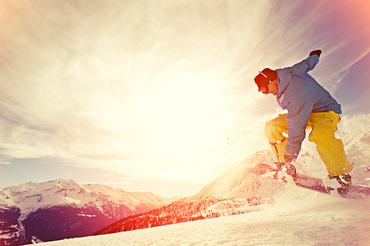 A man snowboarding in the mountains with the sunset in the background.