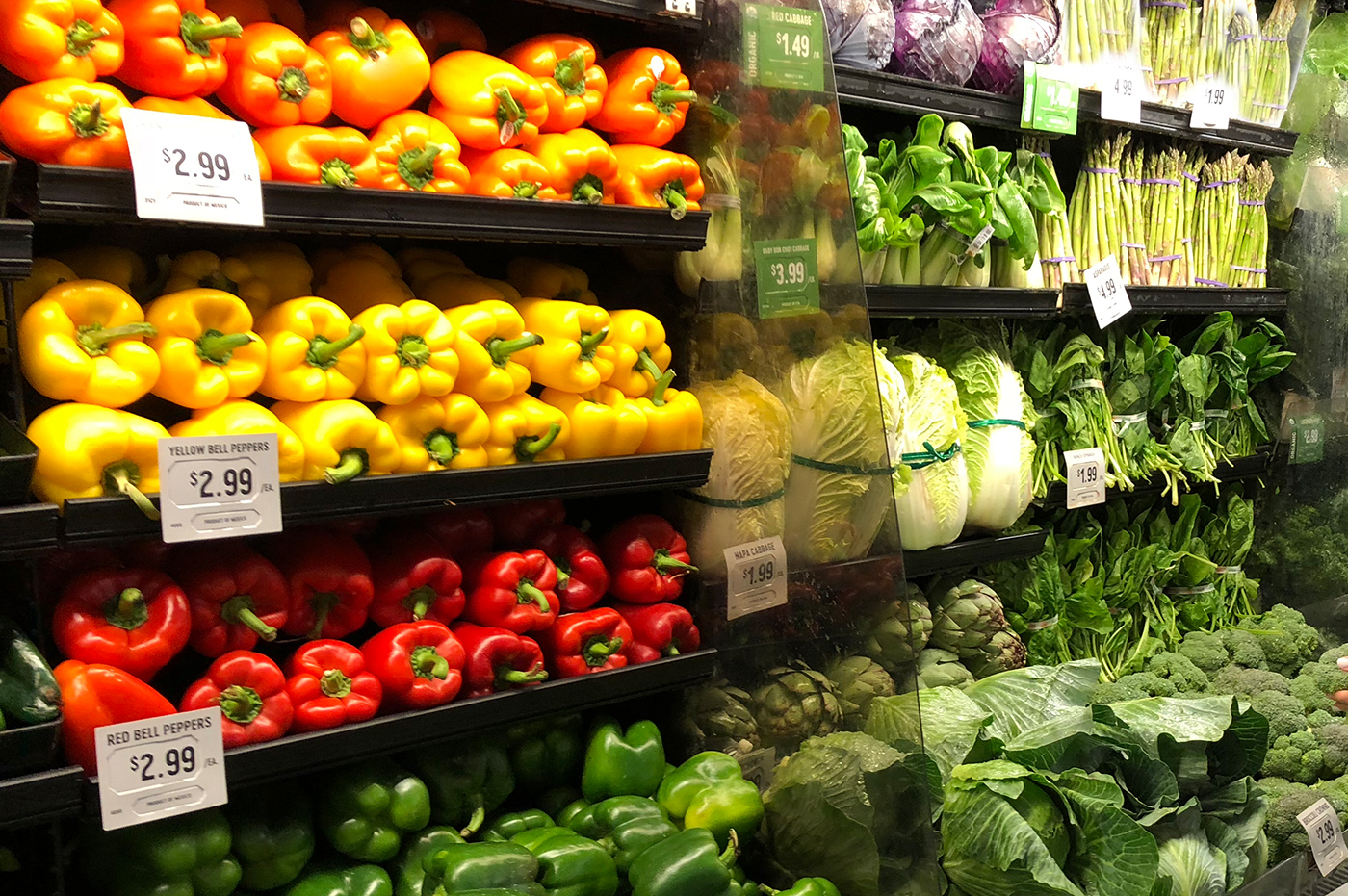 Store produce shelves with peppers and leafy green vegetables.